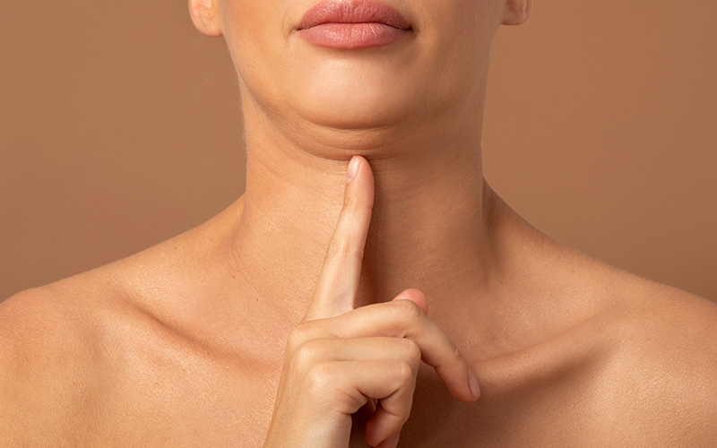 Woman pointing to sagging jawline for aesthetic skin assessment.