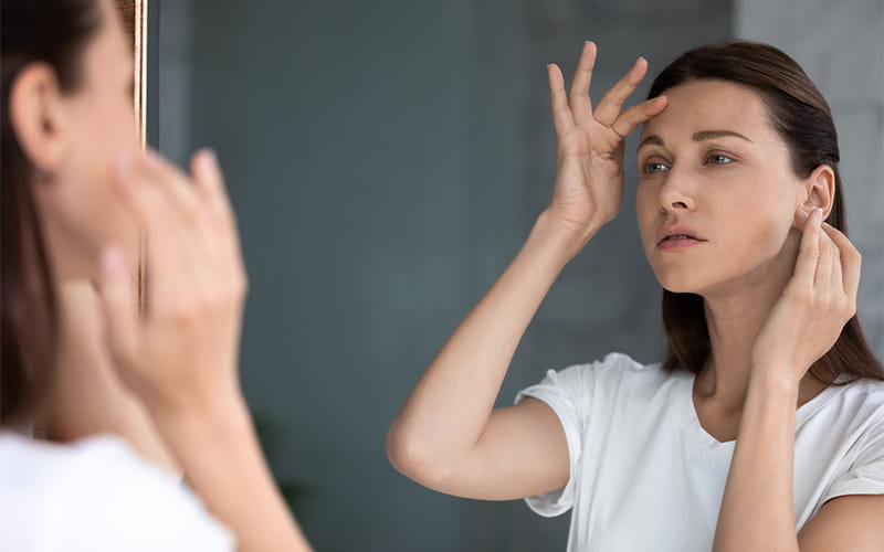 woman looking at her skin in the mirror
