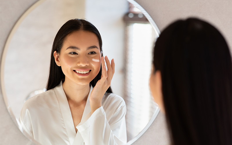 Smiling woman applying protective skincare cream in the mirror.