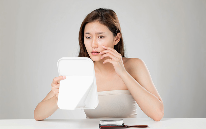 Woman examining skin irritation caused by environmental stressors.