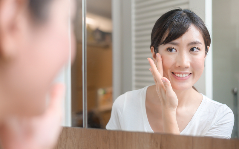 Young-woman-examining-under-eye-area-in-mirror-for-dark-circles