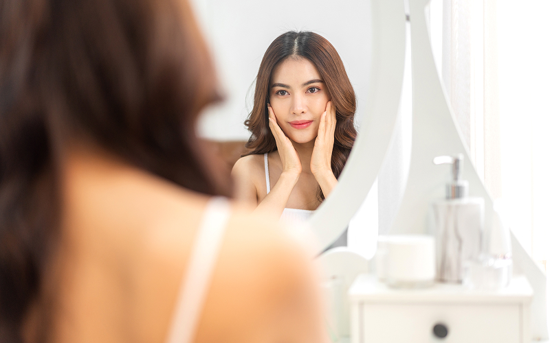Woman touching face admiring healthy skin in vanity mirror.