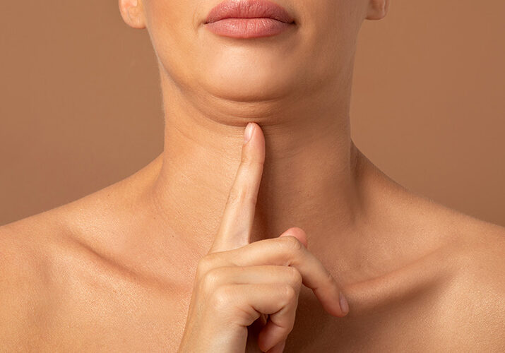 Woman pointing to sagging jawline for aesthetic skin assessment.