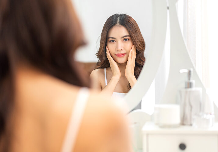 Woman touching face admiring healthy skin in vanity mirror.